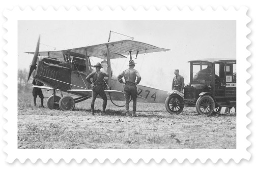 An early-20th century black-and-white photograph of an airplane with four men standing nearby.